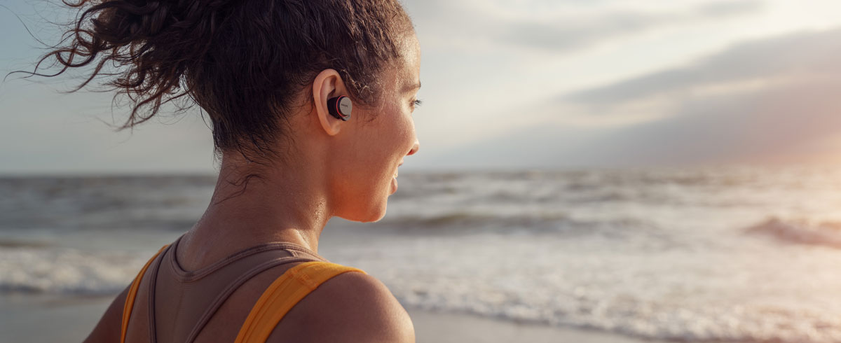 Kobieta nosząca sportowe słuchawki bezprzewodowe true wireless Philips na plaży