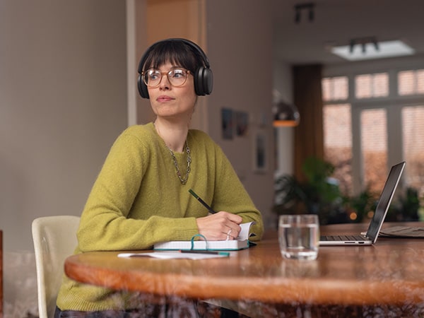 Osoba nosząca wygodne słuchawki Philips siedzi przy stole z notatnikiem i laptopem