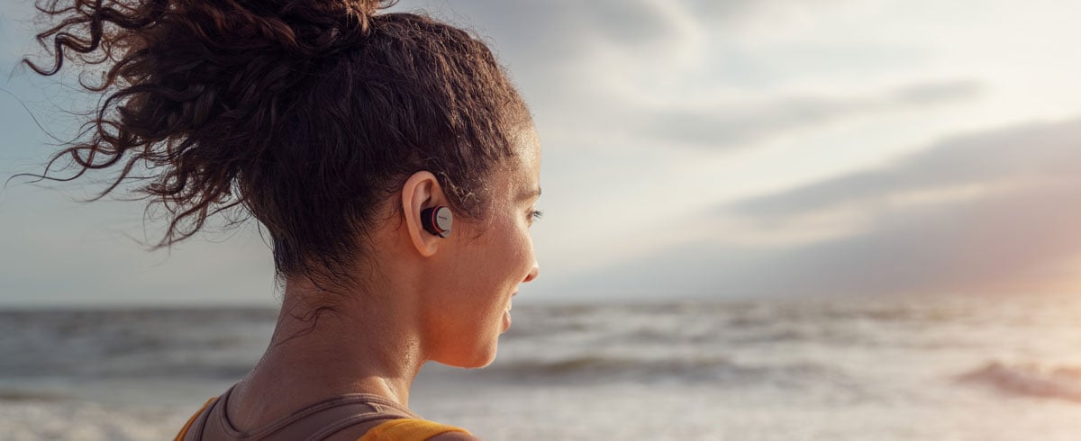 Kobieta korzystająca ze słuchawek bezprzewodowych true wireless nad morzem