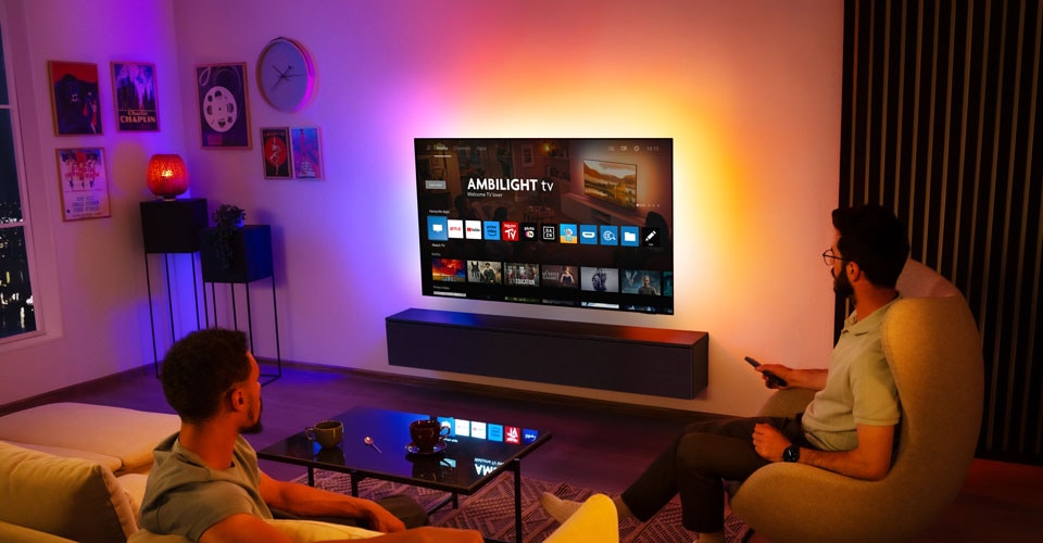 Dwóch mężczyzn ogląda telewizję Ambilight zamontowaną na ścianie w salonie