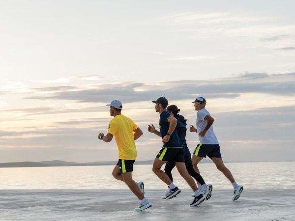 Czterech uczestników biegu wspólnie biegnących po plaży.