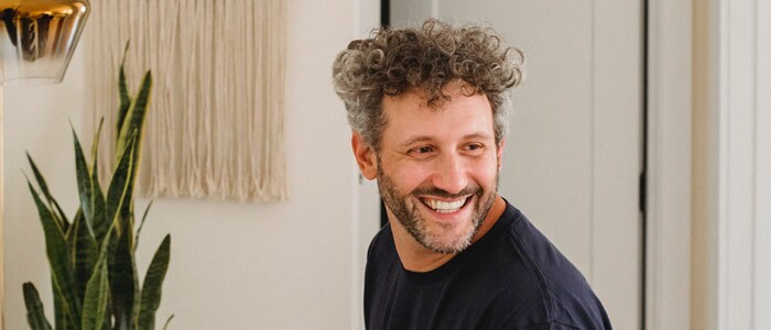 A smiling man with dark, greying curls and a trimmed grey beard sits at a keyboard.