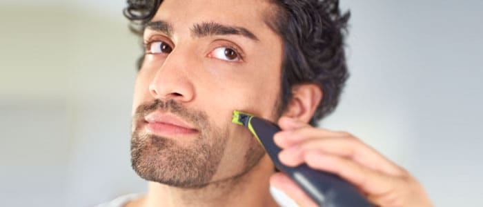 Mężczyzna minimalnie przycina brodę za pomocą trymera ze specjalną końcówką.