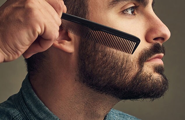 Profil boczny mężczyzny z pełną brodą, który zaczesuje włosy na policzki.