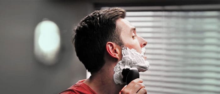 Mężczyzna z pianką do golenia na twarzy, goli się elektryczną maszynką do golenia.