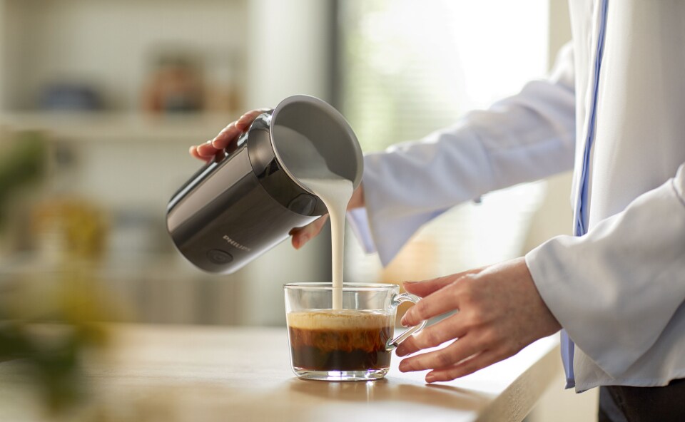 Barista nalewa spienione mleko roślinne do kawy.