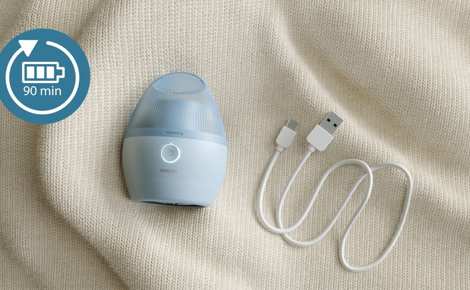 Mała niebieska golarka wraz z kablem USB leżą na swetrze.