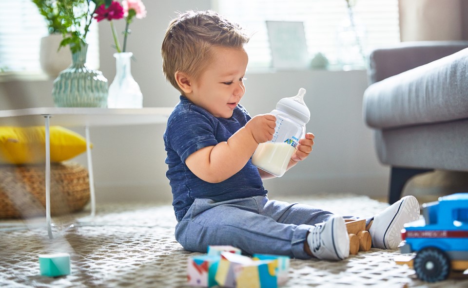Siedzące dziecko bawiące się butelką.