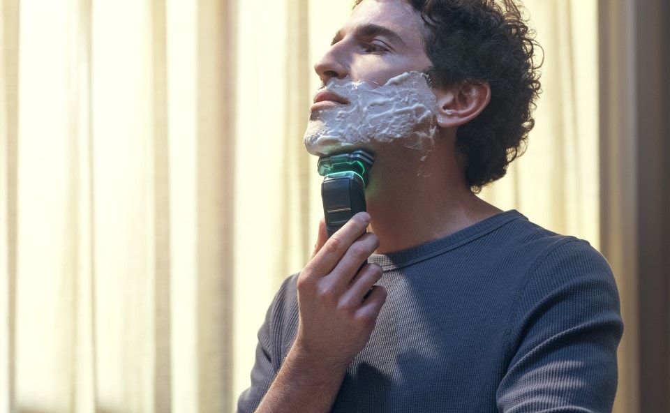 Mężczyzna golący siwą brodę golarką do twarzy Philips.