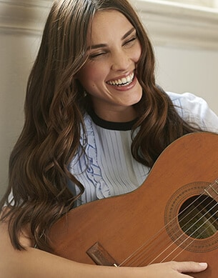 Uśmiechnięta kobieta grająca na gitarze z zadbanymi włosami