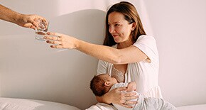 Kobieta sięgająca po szklankę wody w trakcie karmienia piersią